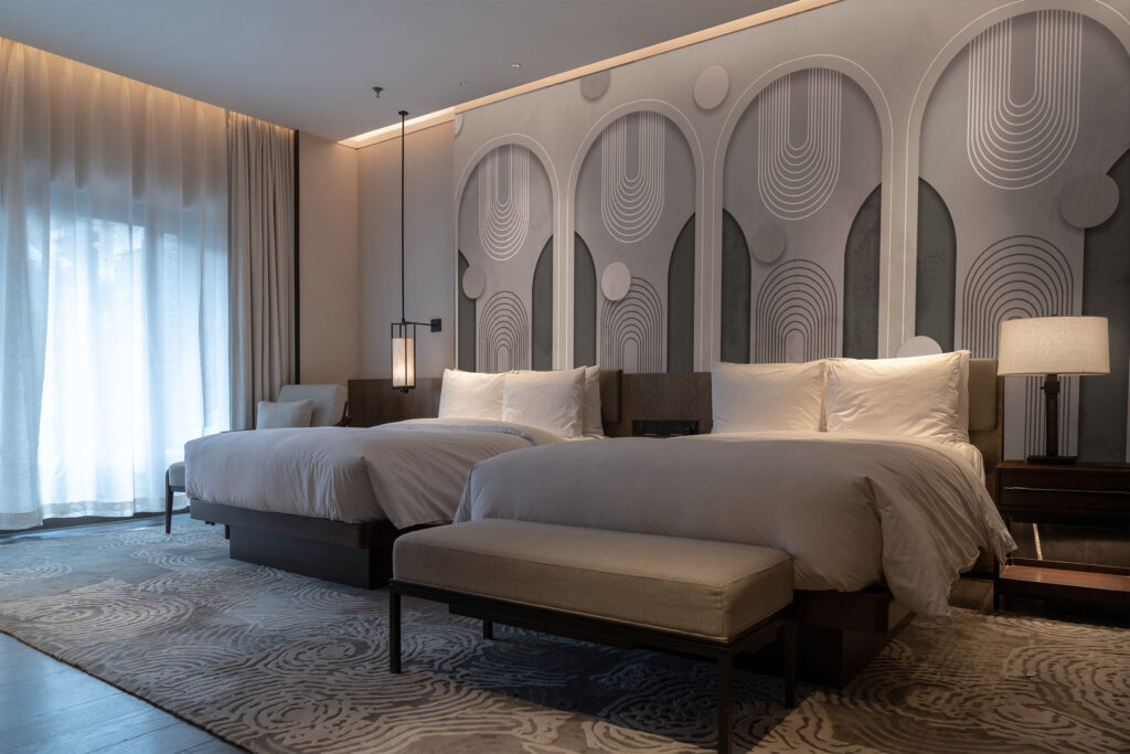 Art deco-style mural wallpaper with arched geometric patterns in grey tones behind modern cream furniture in a hotel room. Baubauwall Wallpapers